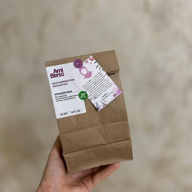 Крафтовый пакет AmiBers в руке: белая этикетка крема для лица со значком ECO и бумажный вкладыш с описанием